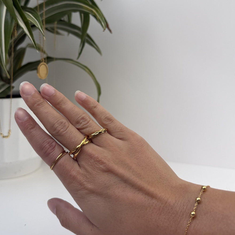 A hand wearing the Thread Ring, Spinner Ring and Double Ring in gold with the Slider Bracelet at the wrist